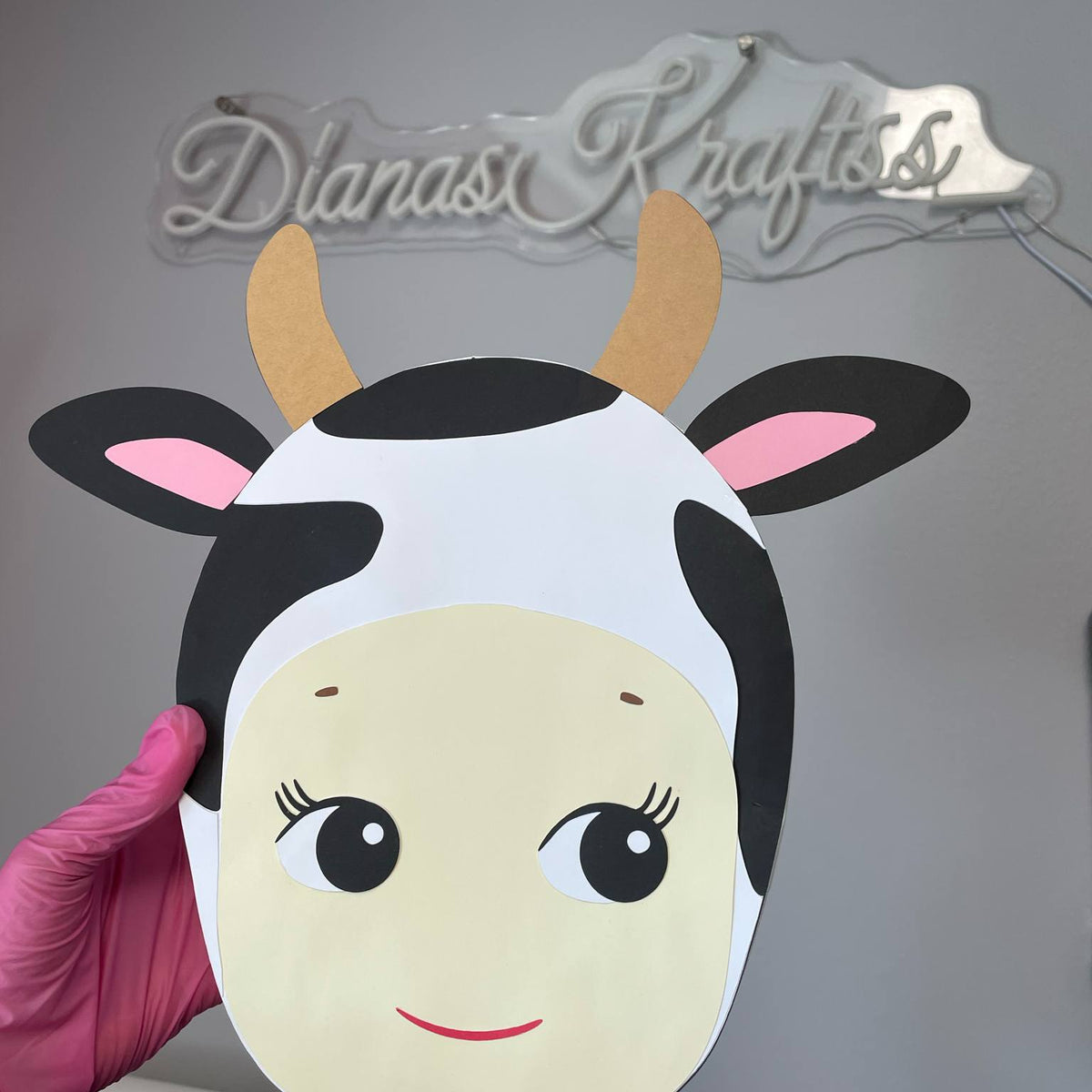 Cow mask with black and white pattern held by a hand against a gray background with 'Dianas Krafts' branding.
