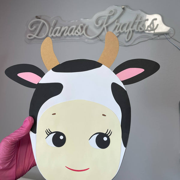 Cow mask with black and white pattern held by a hand against a gray background with 'Dianas Krafts' branding.